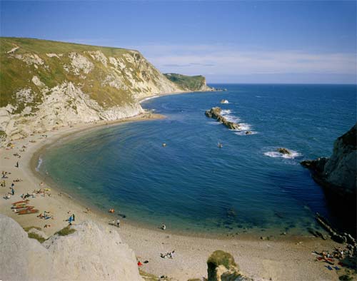 Many beaches are narrow at high tide and wide at low tide. Man o' War Rocks and Cove, and St Oswald's Bay, from Durdle headland, Dorset, UK